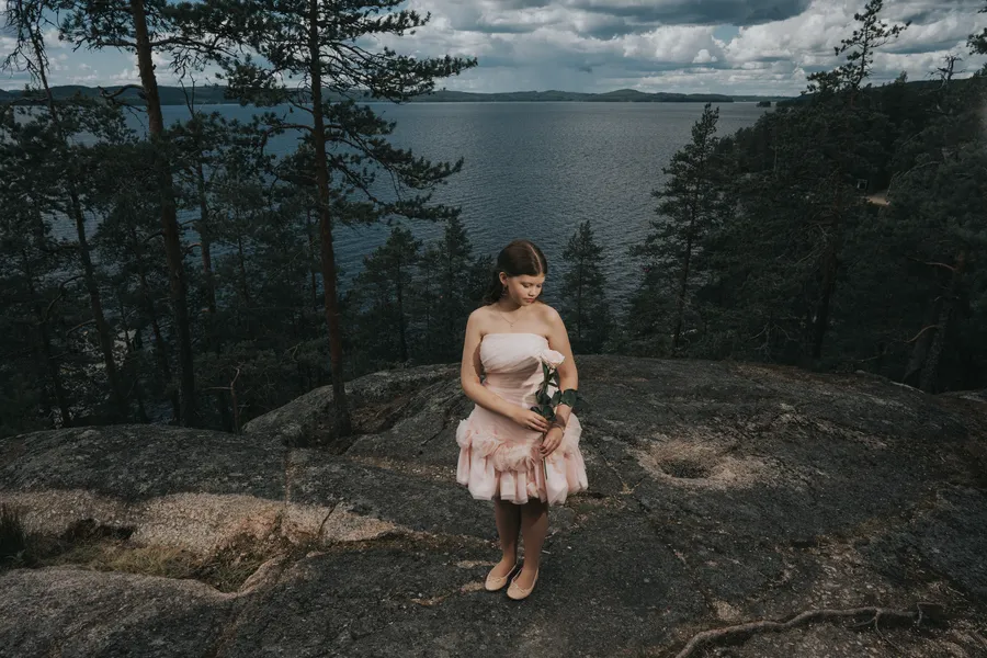 Valmistuja pinkissä mekossa kalliolla järven rannalla