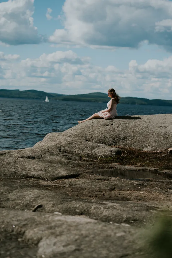 Valmistuja istuu kalliolla järven äärellä