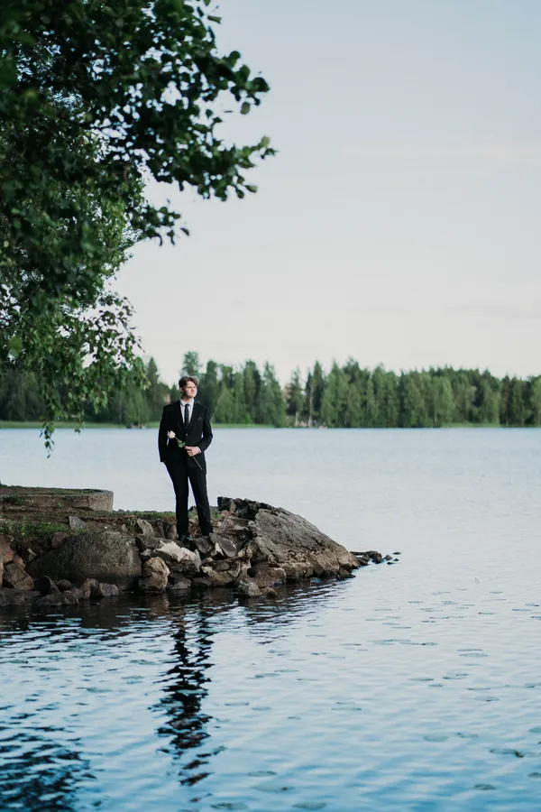 Valmistuja puvussa järven rannalla kalliolla