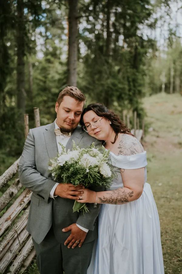 Hääpari halaa ulkona kukkakimppu kädessä