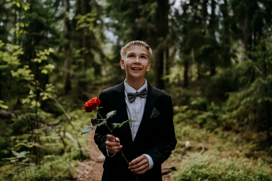 Nuori mies puvussa ja punainen ruusu kädessä metsässä